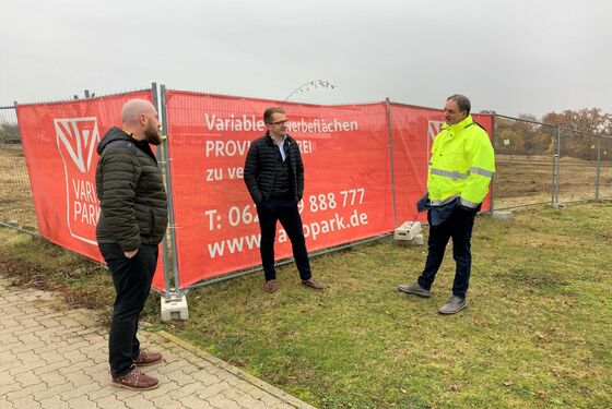 Drei Projektbeteiligte vor Banner-Werbung am Baufeld in Frankenthal